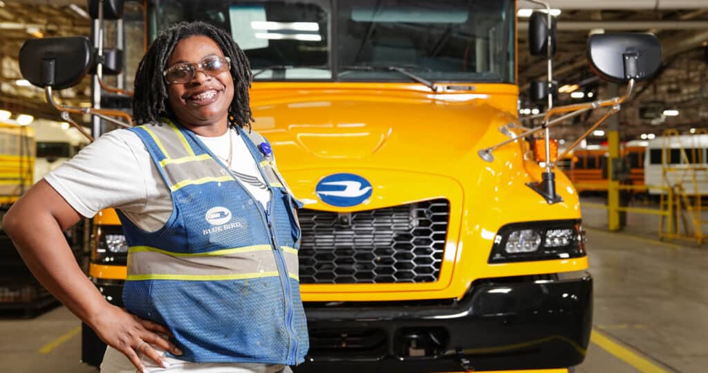 Blue Bird union member smiling and standing with hands on her hips in front of a finished school bus with the Blue Bird logo